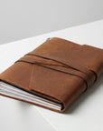 Brown leather notebook with string closure on a white surface