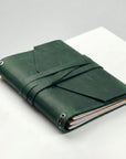 Green leather-bound notebook on a white surface with a gray background