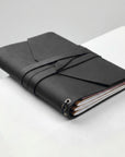 Black leather-bound notebook with a strap on a white surface