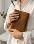 Person holding a brown leather notebook with a light background