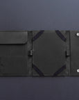 A dark gray leather tablet sleeve or folio case, shown open to display its interior compartments, elastic straps, and snap-button closure on a dark gray background.