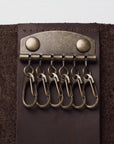 A close-up of a dark brown leather key ring holder with five brass key rings attached to a metal clip with two round rivets.