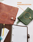 Brown leather planner with open pages, pen, and cards on a white surface with a green planner in the background.