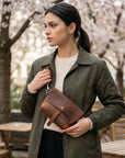 Woman holding a brown leather bag outdoors with cherry blossom trees in the background
