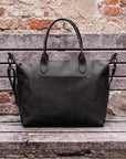 Black leather bag on a wooden surface with a brick wall background