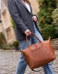 Person holding a brown leather bag on a cobblestone street