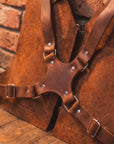 Brown leather harness with metal studs against a brick wall.