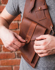 Person holding a brown leather bag against a brick wall