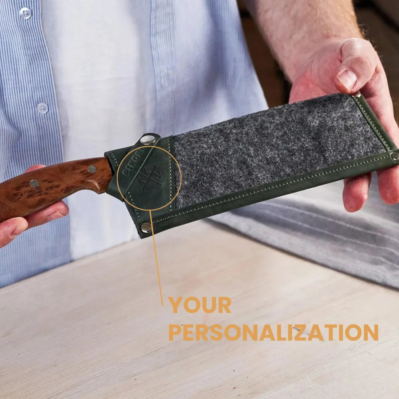 Person holding a knife with a wooden handle and a gray sheath, with text 'Your Personalization' on a wooden surface.