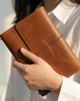 Brown leather notebook held by a person wearing a white shirt.