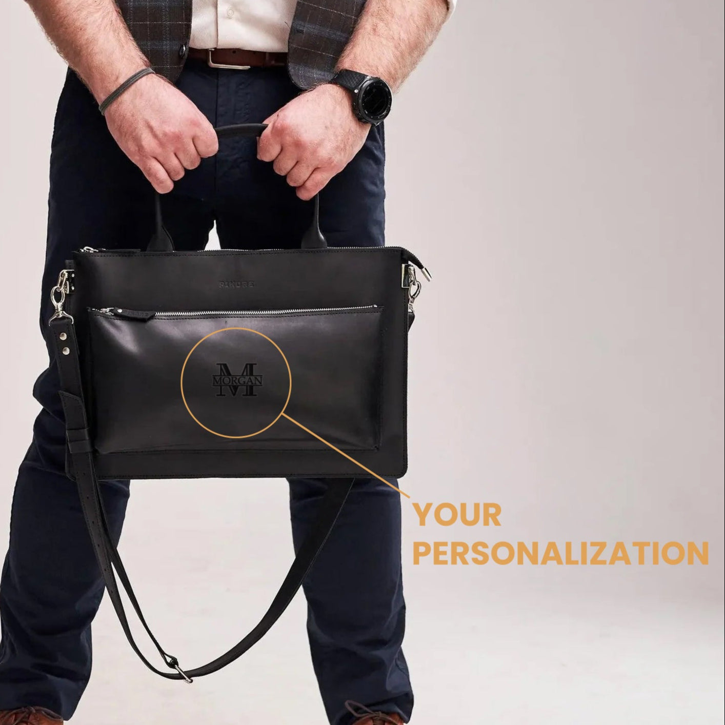 Person holding a black leather bag with customization text on a plain background