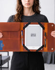 A woman holds open a brown leather folio-style tablet sleeve with a white Onyx Book e-reader inside, plus pens in pockets, against an indoor room background.