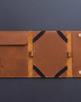A brown leather organizer sleeve or folio, shown open flat against a dark gray background. The interior features multiple pockets, elastic black straps, and silver metal snap buttons on the right side.