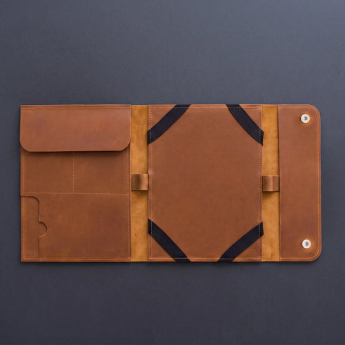 A brown leather organizer sleeve or folio, shown open flat against a dark gray background. The interior features multiple pockets, elastic black straps, and silver metal snap buttons on the right side.