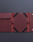 A dark reddish-brown leather travel organizer sleeve, shown open to reveal multiple pockets, elastic bands, and snap-button closure on a dark gray background.
