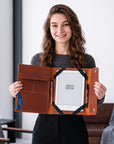 A woman holds open a brown leather book sleeve containing a white Onyx Book, with pen loops, card slots, and pockets visible, in a modern indoor setting.