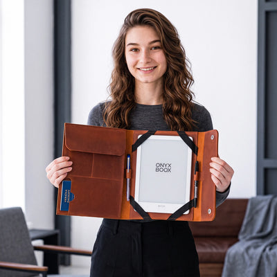 A woman holds open a brown leather book sleeve containing a white Onyx Book, with pen loops, card slots, and pockets visible, in a modern indoor setting.