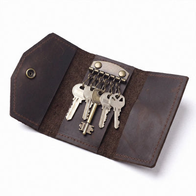 A dark brown leather key organizer case shown open on a white background, holding several metal keys attached to a brass-toned key ring.