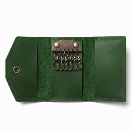A dark green leather keyring roll-up case shown open on a white background, featuring multiple metal key rings and a snap-button closure.