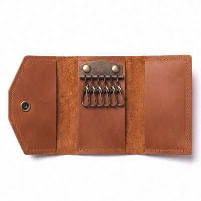 A brown leather key holder wallet shown open on a white background, featuring six metal key rings attached to a brass-tone clasp and a snap button closure on the left.