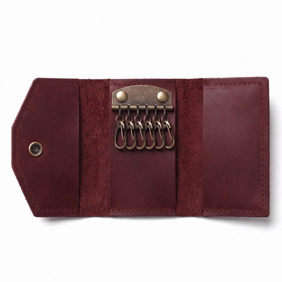 A round burgundy faux-suede crossbody bag with geometric paneling and a matching adjustable shoulder strap, displayed on a clean white background.