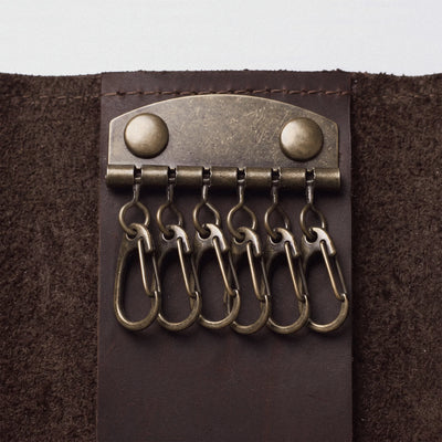 A close-up of a dark brown leather key ring holder with five brass key rings attached to a metal clip with two round rivets.