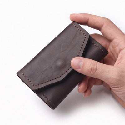 A dark brown leather card holder or wallet with visible stitching, held in a person's hand against a plain white background.