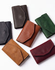 Six leather card holders in different colors (black, brown, tan, green, burgundy) arranged on a plain white background.
