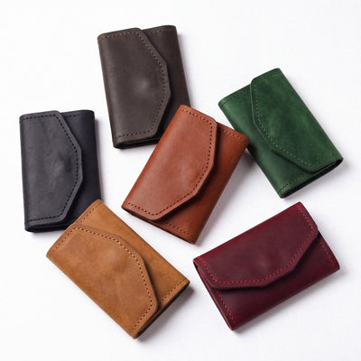 Six leather card holders in different colors (black, brown, tan, green, burgundy) arranged on a plain white background.