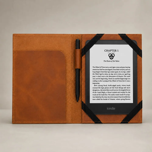 A tan leather folio-style Kindle case shown open on a light neutral background, with a black pen in a side pocket and a Kindle e-reader partially inserted on the right side.