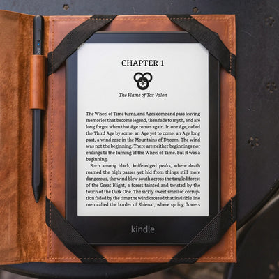 A Kindle e-reader device in a brown leather folio case, displaying a book chapter on a dark textured surface.