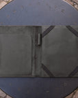 A dark olive green leather portfolio folder shown open, resting on a round black metal patio table with a stone paver floor visible in the background.