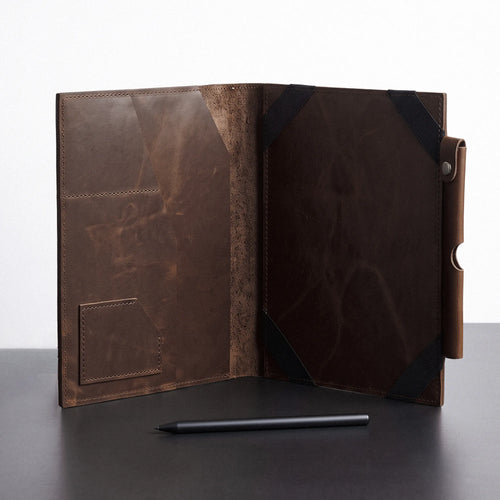 A dark brown distressed leather folio case shown open, displaying its interior pockets and texture, with a black stylus resting in front on a dark surface against a white background.