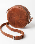 A brown leather crossbody bag with a circular body, geometric stitched panel design, and a detachable adjustable strap, shown on a light gray background.