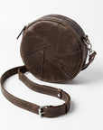 A dark brown distressed leather crossbody bag with a circular body, geometric stitched panel design, and a matching adjustable leather strap with a silver buckle, shown on a light gray background.