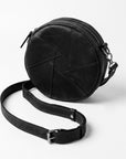 A black round leather crossbody bag with geometric stitched paneling and a detachable shoulder strap, photographed on a clean white background.