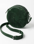 A dark green circular crossbody bag made of textured leather with geometric stitched paneling, shown with its matching adjustable shoulder strap on a light gray background.