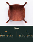 A square copper-colored leather tray with four raised corners, shown from above on a white background, with a dark green size chart below detailing measurements for M and L sizes.