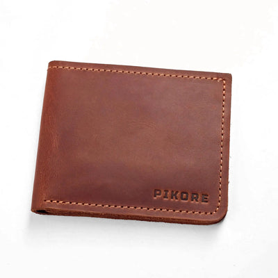 A brown leather bifold wallet with visible stitching and the brand name 'PIKORE' embossed in the bottom right corner, shown on a plain white background.