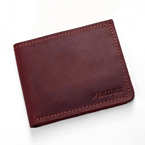 A dark reddish-brown leather bifold wallet with visible stitching and the brand name 'PIKORE' debossed on the bottom right, shown on a clean white background.