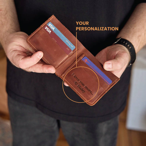 Person holding a brown leather wallet with personalized engraving, showing Visa cards inside.