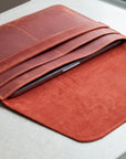 A reddish-brown leather tablet sleeve or folio case with multiple card slots, shown open on a light gray surface. A tablet is partially tucked inside.