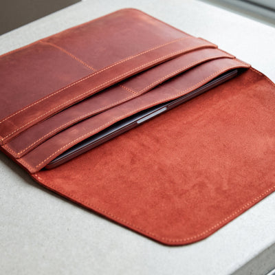 A reddish-brown leather tablet sleeve or folio case with multiple card slots, shown open on a light gray surface. A tablet is partially tucked inside.