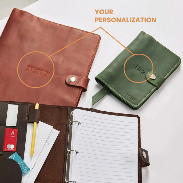 Brown leather planner with open pages, pen, and cards on a white surface with a green planner in the background.