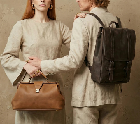Two people in vintage-style clothing with a brown leather bag and a dark backpack.