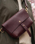 Brown leather bag with gold accents on a person wearing a green coat.