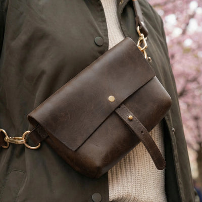 Brown leather bag with gold accents on a person wearing a dark coat and beige sweater.
