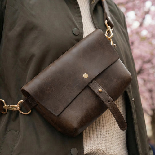 Brown leather bag with gold accents on a person wearing a dark coat and beige sweater.
