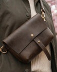 Brown leather bag with gold accents on a person wearing a dark coat and beige sweater.