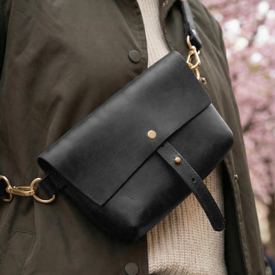 Black leather bag with gold accents on a person wearing a coat and sweater.